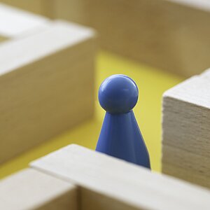 Eine blaue Spielfigur steht in einem Holzlabyrinth