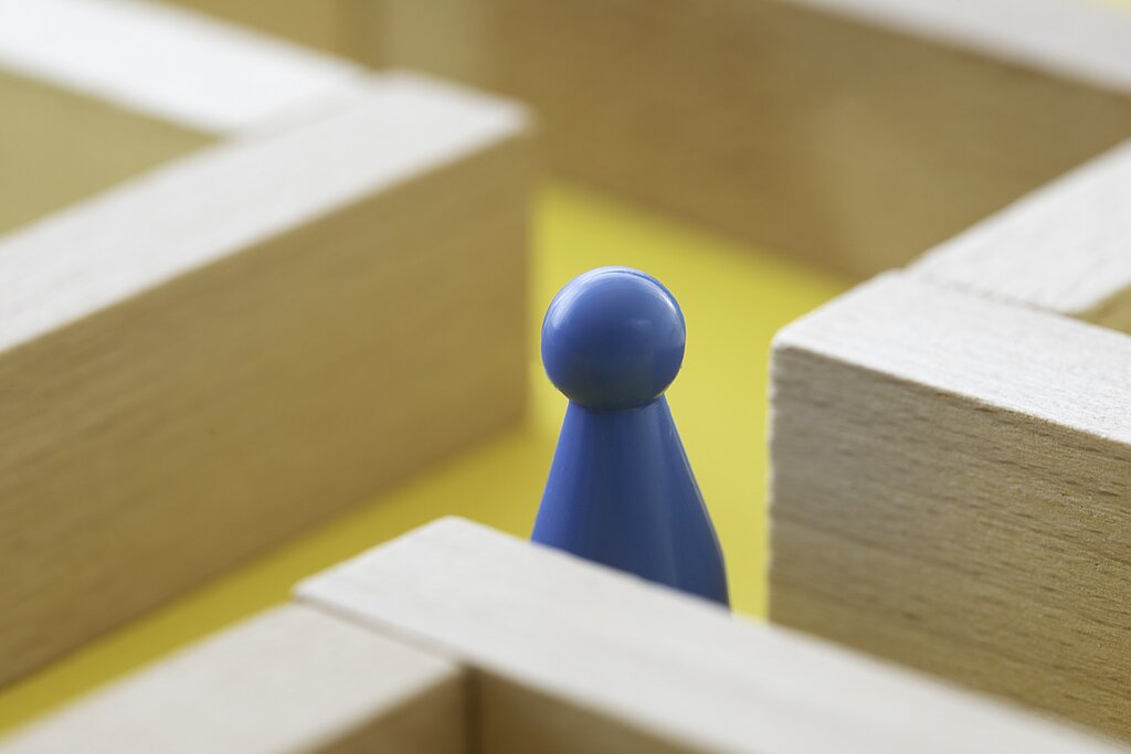 Eine blaue Spielfigur steht in einem Holzlabyrinth