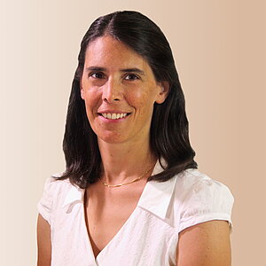 Eine Frau mit dunklen, schulterlangen Haaren lächelt freundlich in einer hellen Umgebung in die Kamera.